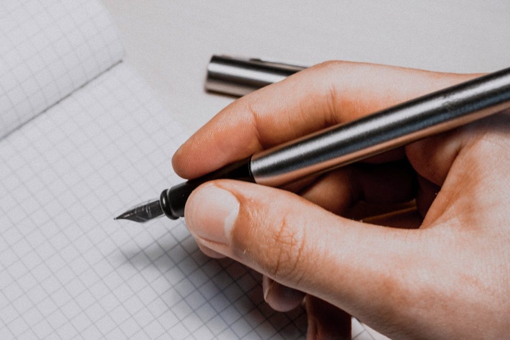 A detailed shot of a hand holding a fountain pen over graphing paper, suggesting creativity and planning.